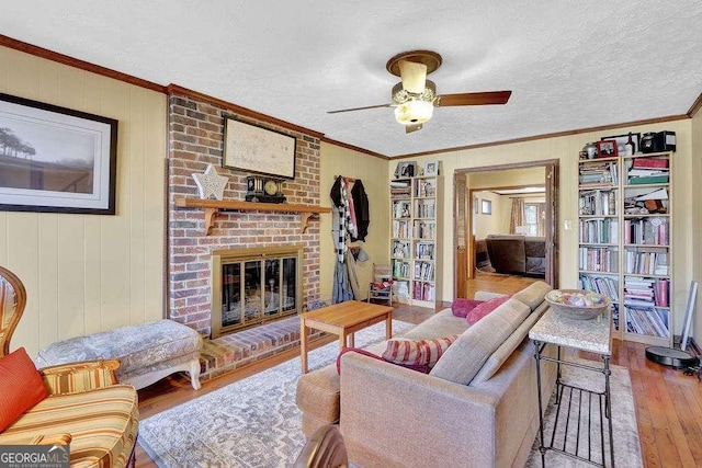 living room with crown molding, ceiling fan, a textured ceiling, a fireplace, and light hardwood / wood-style floors