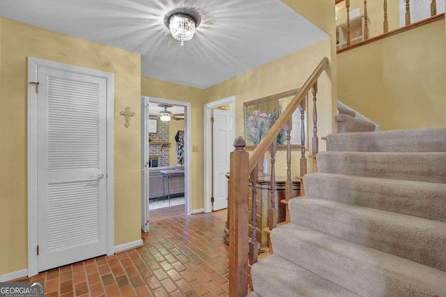 stairway featuring a brick fireplace and ceiling fan