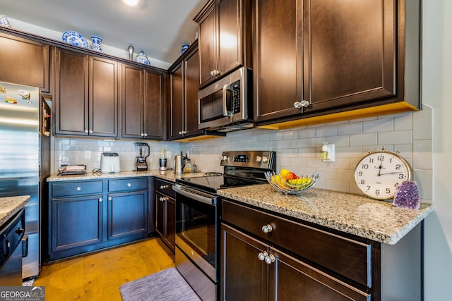 kitchen with dark brown cabinets, light hardwood / wood-style floors, light stone countertops, and stainless steel appliances