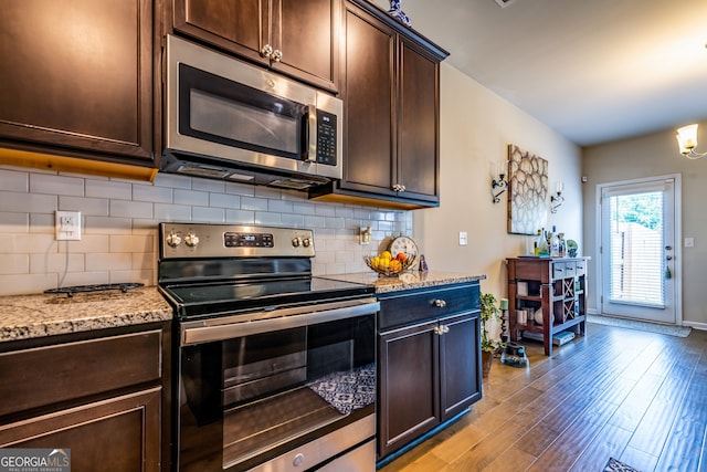 kitchen featuring stainless steel appliances, tasteful backsplash, light stone counters, light hardwood / wood-style floors, and dark brown cabinets