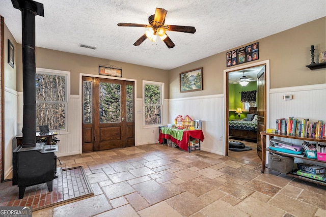 foyer entrance with a wood stove, ceiling fan, and a textured ceiling