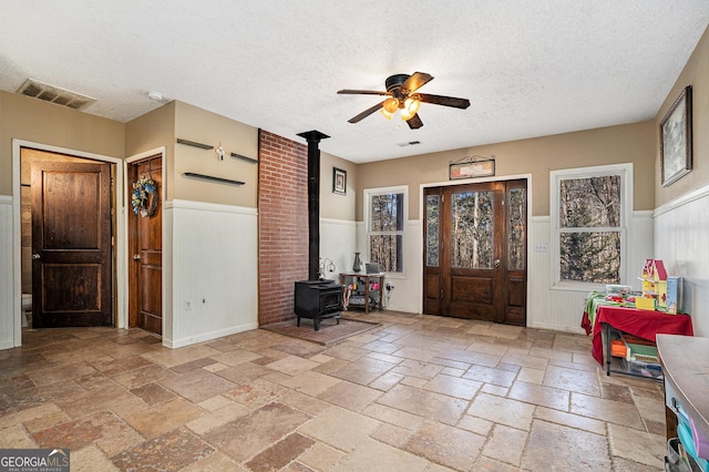 entryway featuring a wood stove, ceiling fan, and a textured ceiling