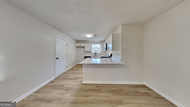 kitchen with kitchen peninsula, stove, a textured ceiling, light hardwood / wood-style flooring, and white cabinetry