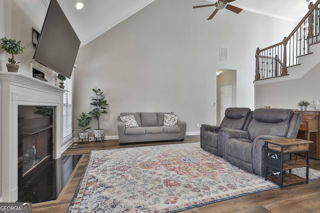 living room with ceiling fan, a towering ceiling, ornamental molding, and dark hardwood / wood-style floors