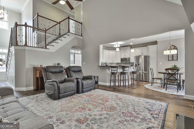 living room with ceiling fan, a high ceiling, dark hardwood / wood-style flooring, and crown molding