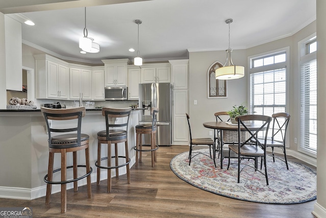 kitchen with appliances with stainless steel finishes, pendant lighting, ornamental molding, and white cabinets