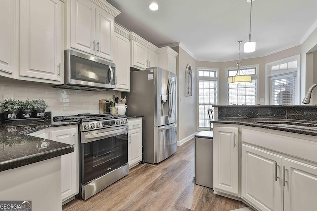 kitchen with appliances with stainless steel finishes, white cabinetry, dark stone countertops, sink, and hanging light fixtures