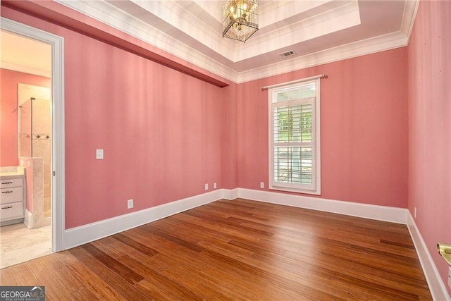 empty room featuring hardwood / wood-style floors, an inviting chandelier, a raised ceiling, and crown molding