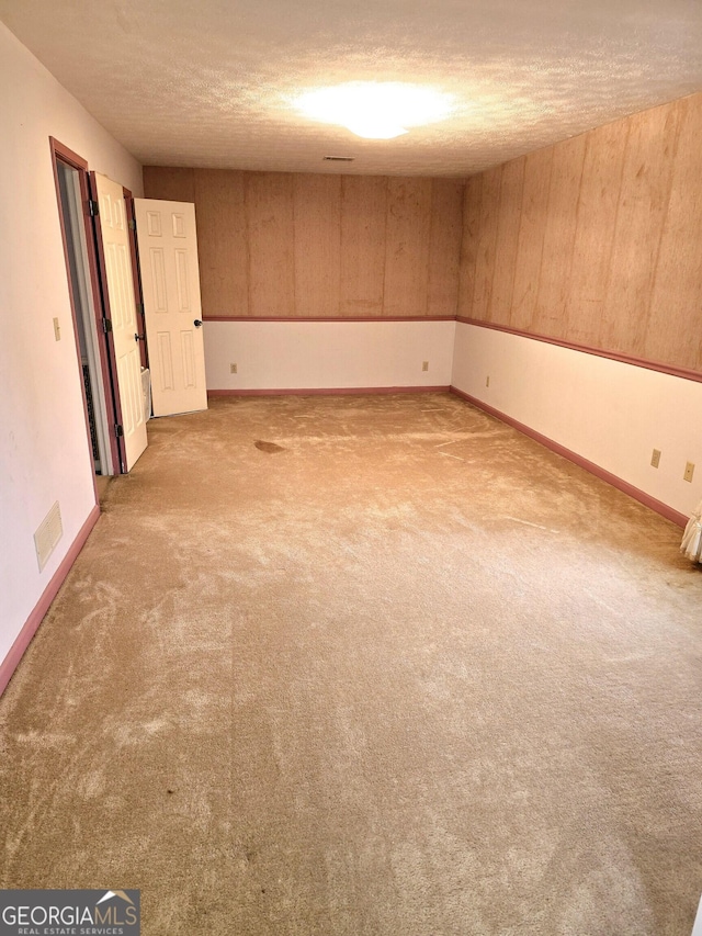 unfurnished room featuring a textured ceiling, carpet floors, and wood walls