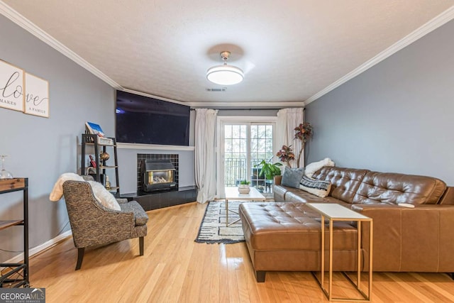 living room with a textured ceiling, light wood-type flooring, crown molding, and a tiled fireplace