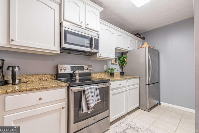 kitchen featuring dark stone countertops, white cabinets, stainless steel appliances, and light tile patterned floors