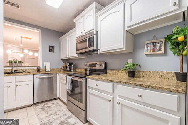 kitchen with white cabinets, sink, light tile patterned floors, appliances with stainless steel finishes, and light stone counters