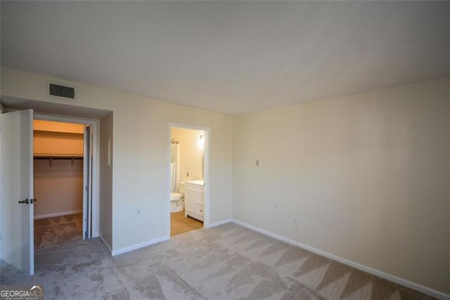 unfurnished bedroom with ensuite bathroom, light colored carpet, a walk in closet, and a closet