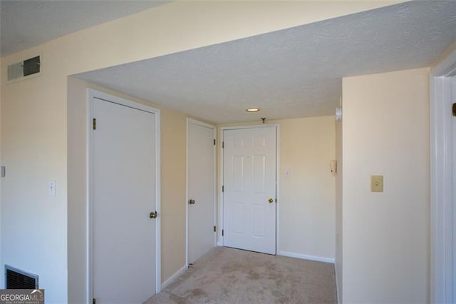 hallway with a textured ceiling and light carpet