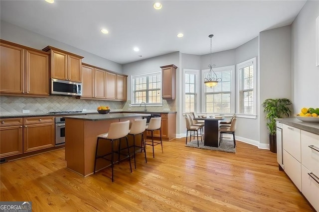 kitchen featuring a center island, pendant lighting, a kitchen bar, appliances with stainless steel finishes, and light wood-type flooring