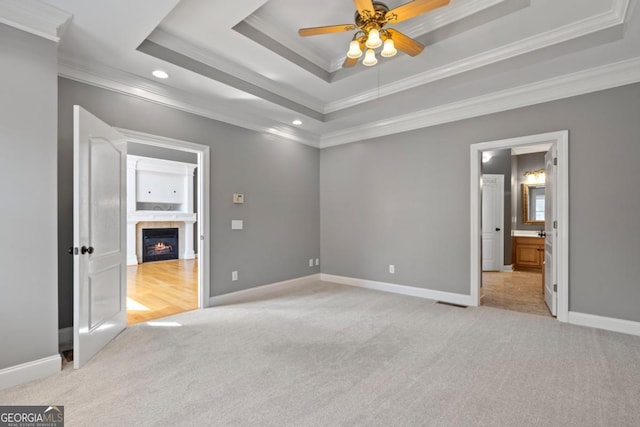 unfurnished bedroom with a raised ceiling, ceiling fan, ornamental molding, connected bathroom, and light colored carpet