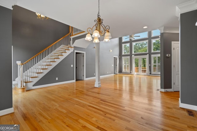 unfurnished living room featuring light wood-type flooring, a towering ceiling, ceiling fan with notable chandelier, and crown molding