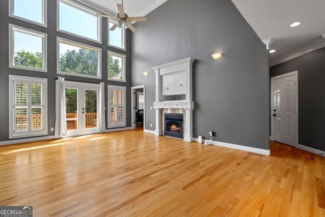 unfurnished living room with a tile fireplace, ceiling fan, a high ceiling, light hardwood / wood-style flooring, and ornamental molding