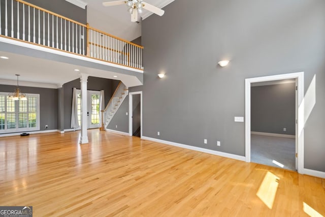 unfurnished living room with decorative columns, ornamental molding, ceiling fan with notable chandelier, light hardwood / wood-style flooring, and a high ceiling