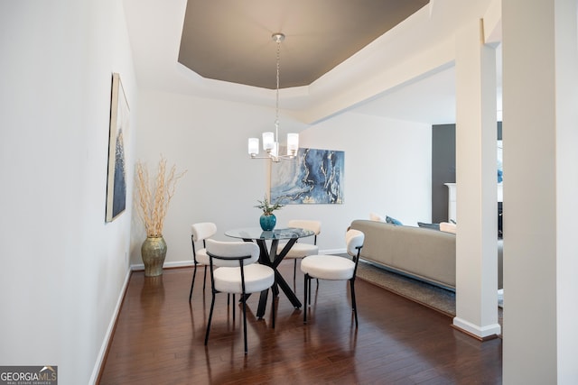 dining area featuring a notable chandelier, a raised ceiling, and dark wood-type flooring