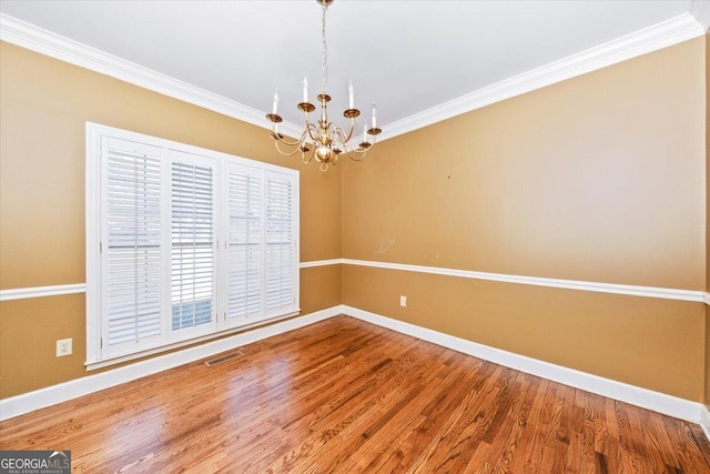 spare room featuring hardwood / wood-style flooring, crown molding, and a notable chandelier