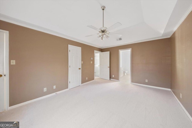 unfurnished bedroom featuring ensuite bathroom, a raised ceiling, ceiling fan, ornamental molding, and light colored carpet