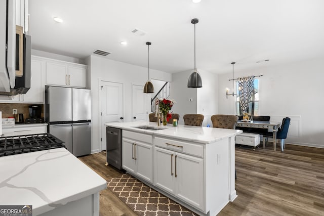 kitchen with stainless steel appliances, a kitchen island with sink, sink, white cabinets, and hanging light fixtures