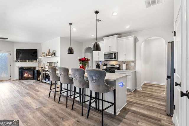 kitchen featuring tasteful backsplash, a kitchen breakfast bar, a center island with sink, white cabinets, and appliances with stainless steel finishes