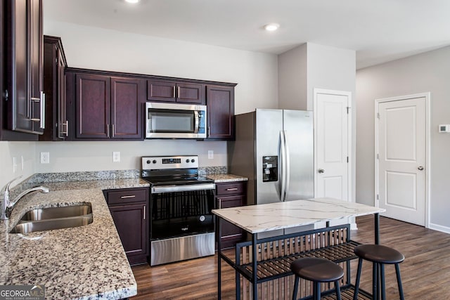 kitchen featuring sink, dark hardwood / wood-style floors, appliances with stainless steel finishes, dark brown cabinets, and light stone counters