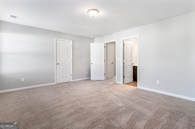 unfurnished bedroom with ensuite bathroom and light carpet