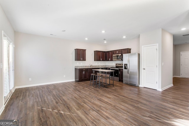 kitchen with a center island, dark hardwood / wood-style flooring, a kitchen bar, dark brown cabinets, and appliances with stainless steel finishes