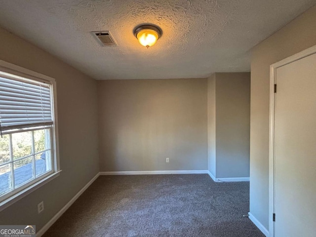 empty room featuring a textured ceiling and dark carpet