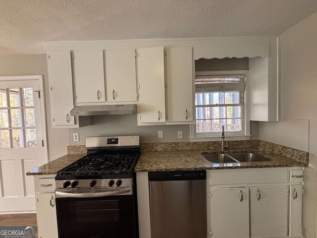 kitchen featuring dark stone countertops, appliances with stainless steel finishes, a textured ceiling, white cabinetry, and sink