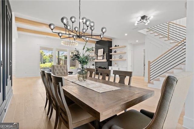 dining space with a large fireplace, an inviting chandelier, and light hardwood / wood-style flooring