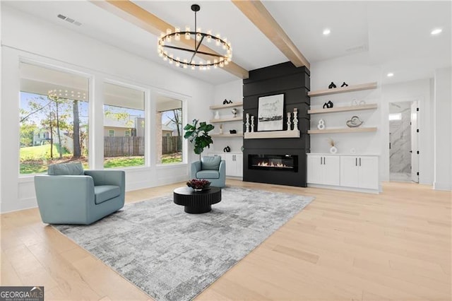 living room featuring a notable chandelier, a large fireplace, light wood-type flooring, and beam ceiling