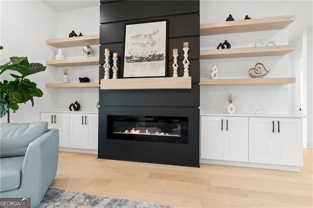 bar with a large fireplace, light hardwood / wood-style floors, and white cabinetry