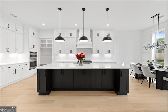 kitchen with stainless steel double oven, premium range hood, white cabinetry, and a large island