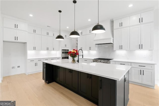 kitchen featuring white cabinets, decorative light fixtures, light hardwood / wood-style floors, and an island with sink