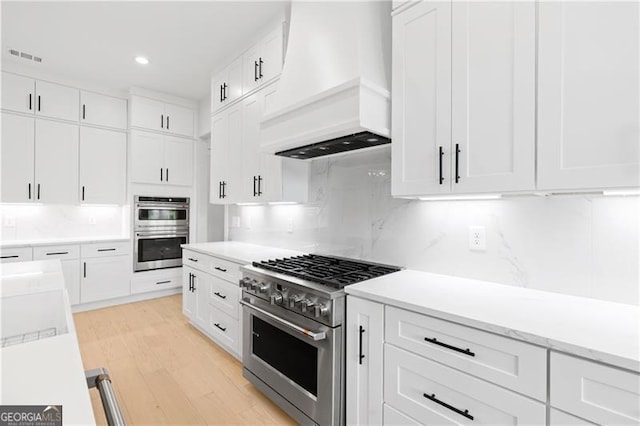 kitchen with light hardwood / wood-style flooring, stainless steel appliances, white cabinetry, and custom exhaust hood