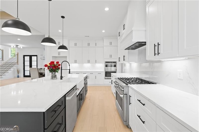 kitchen with a large island with sink, white cabinets, sink, appliances with stainless steel finishes, and decorative light fixtures