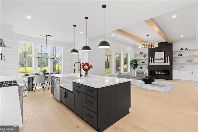 kitchen with sink, decorative light fixtures, a center island with sink, a fireplace, and light hardwood / wood-style floors