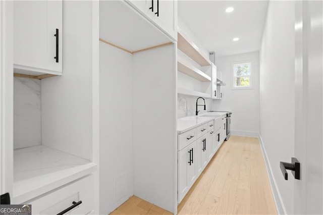 interior space with white cabinets, sink, decorative backsplash, light hardwood / wood-style floors, and light stone counters