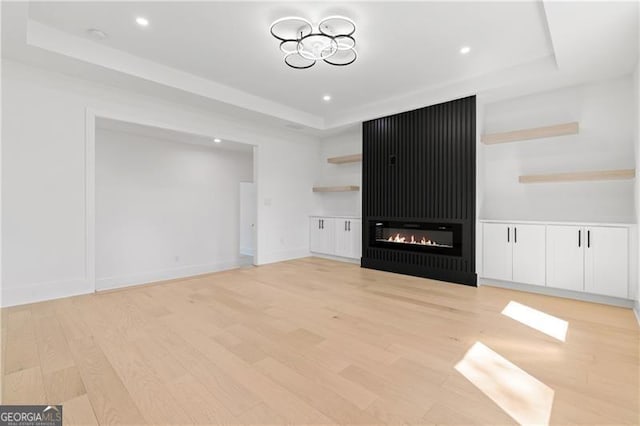 unfurnished living room with a raised ceiling, a fireplace, and light hardwood / wood-style flooring