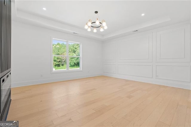 spare room with a raised ceiling, light wood-type flooring, and a chandelier