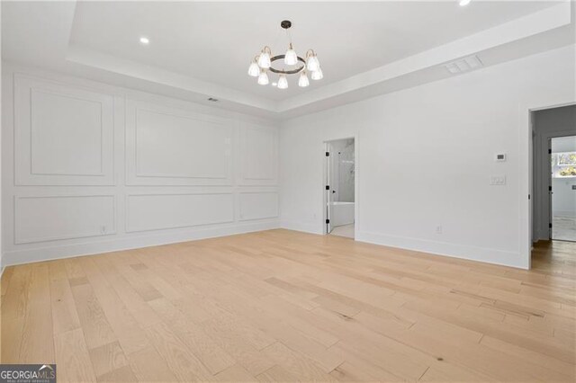 spare room with a chandelier, a tray ceiling, and light hardwood / wood-style floors