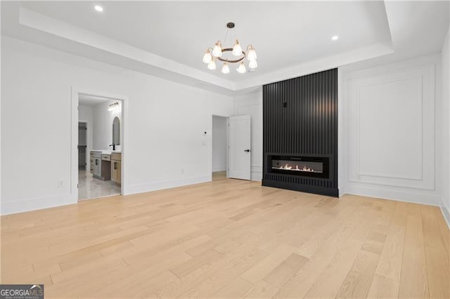 unfurnished living room with a raised ceiling, a fireplace, a chandelier, and light hardwood / wood-style floors