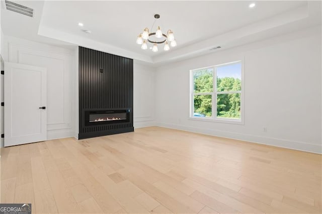 unfurnished living room with a raised ceiling, a fireplace, light hardwood / wood-style floors, and an inviting chandelier