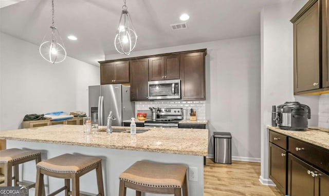 kitchen featuring light stone counters, stainless steel appliances, an island with sink, and tasteful backsplash