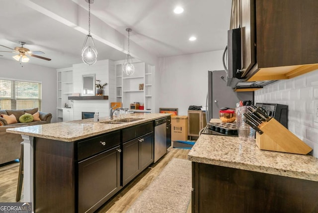 kitchen featuring dark brown cabinetry, dishwasher, sink, decorative light fixtures, and a kitchen island with sink