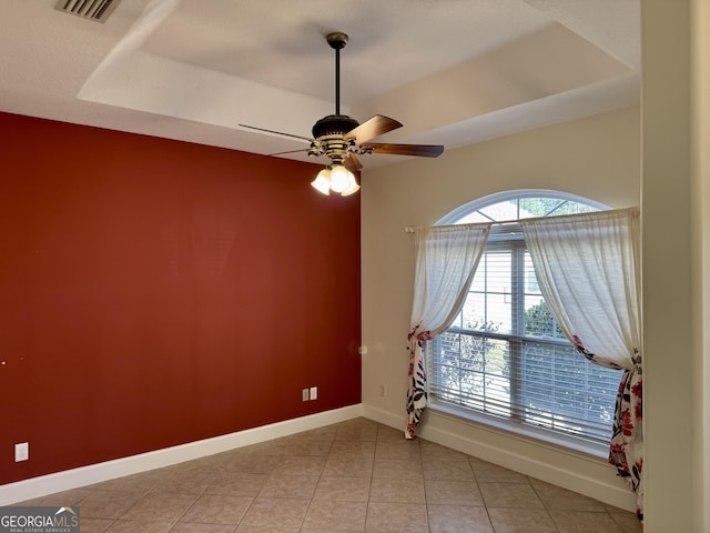 tiled spare room featuring ceiling fan and a raised ceiling